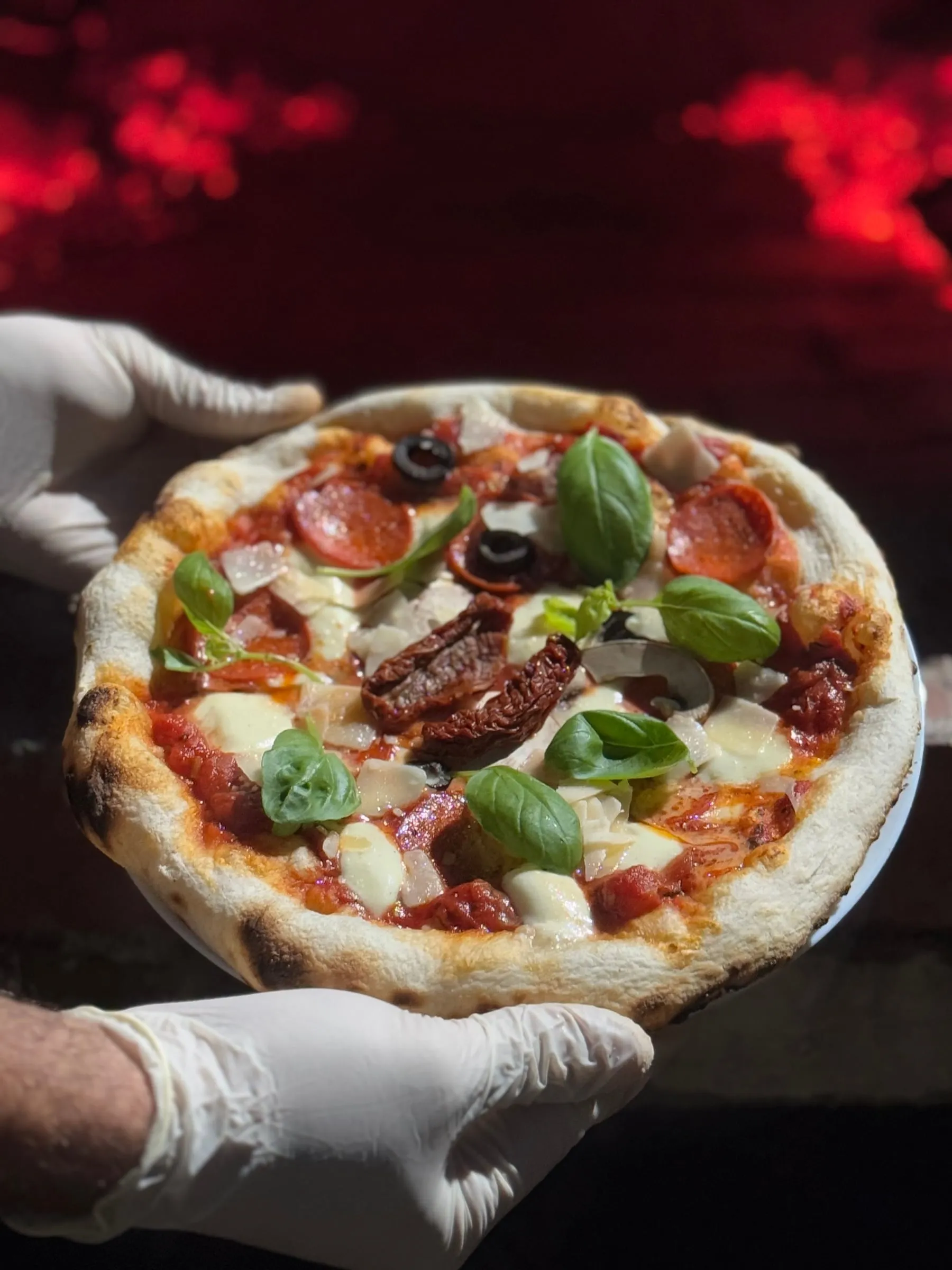 A freshly baked pizza with basil, salami and mozzarella, held in front of a glowing oven