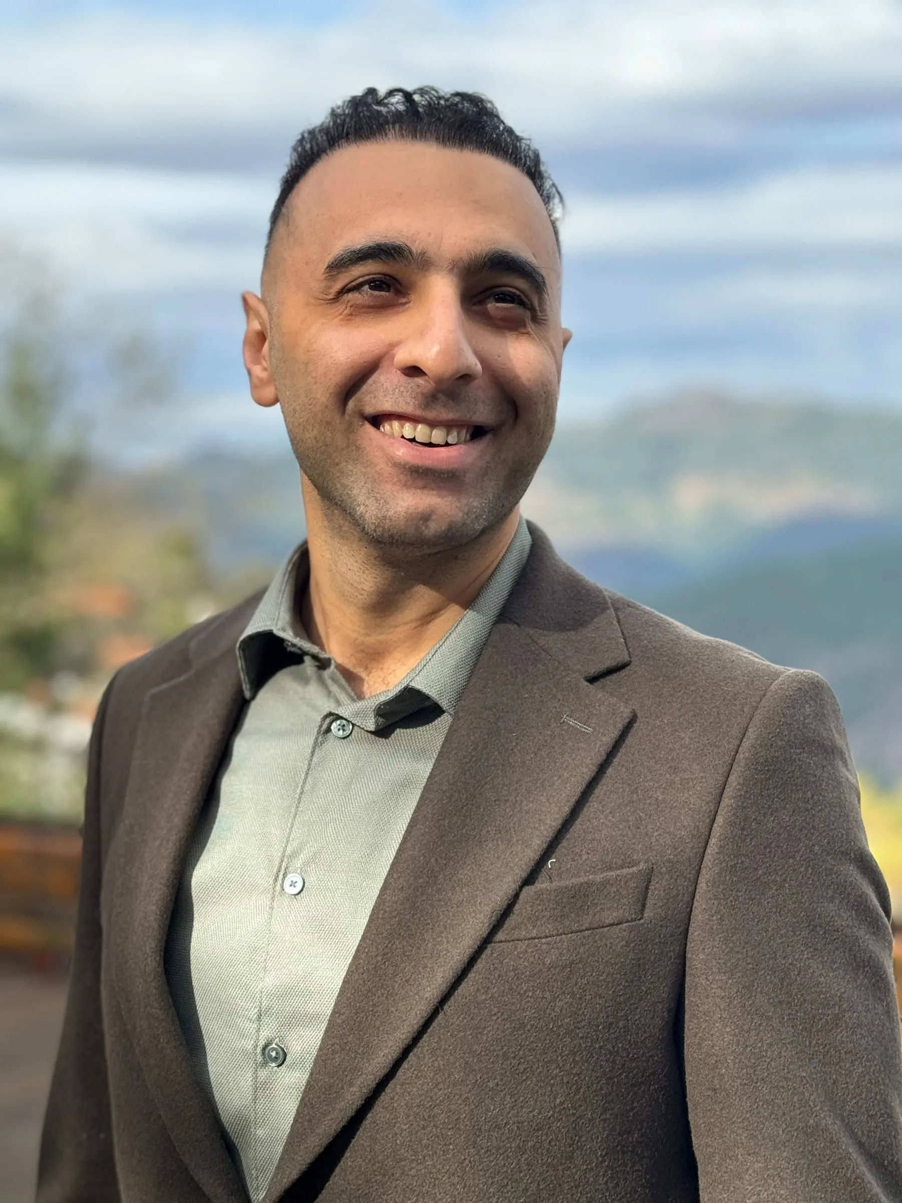 Portrait of Shahin Gharghi smiling outdoors, mountains behind