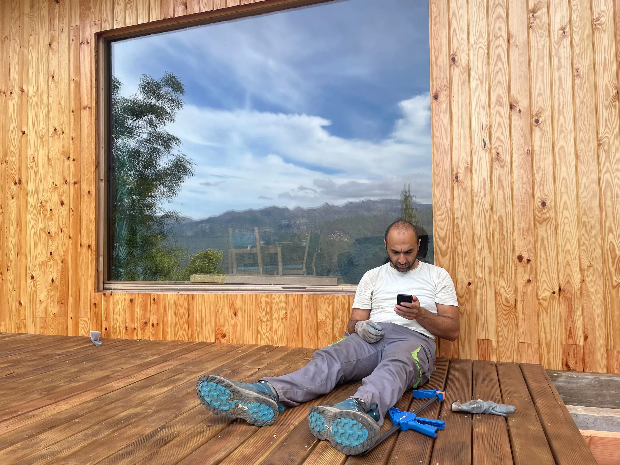 Shahin taking a break on the finished deck in front of a large window reflecting mountains