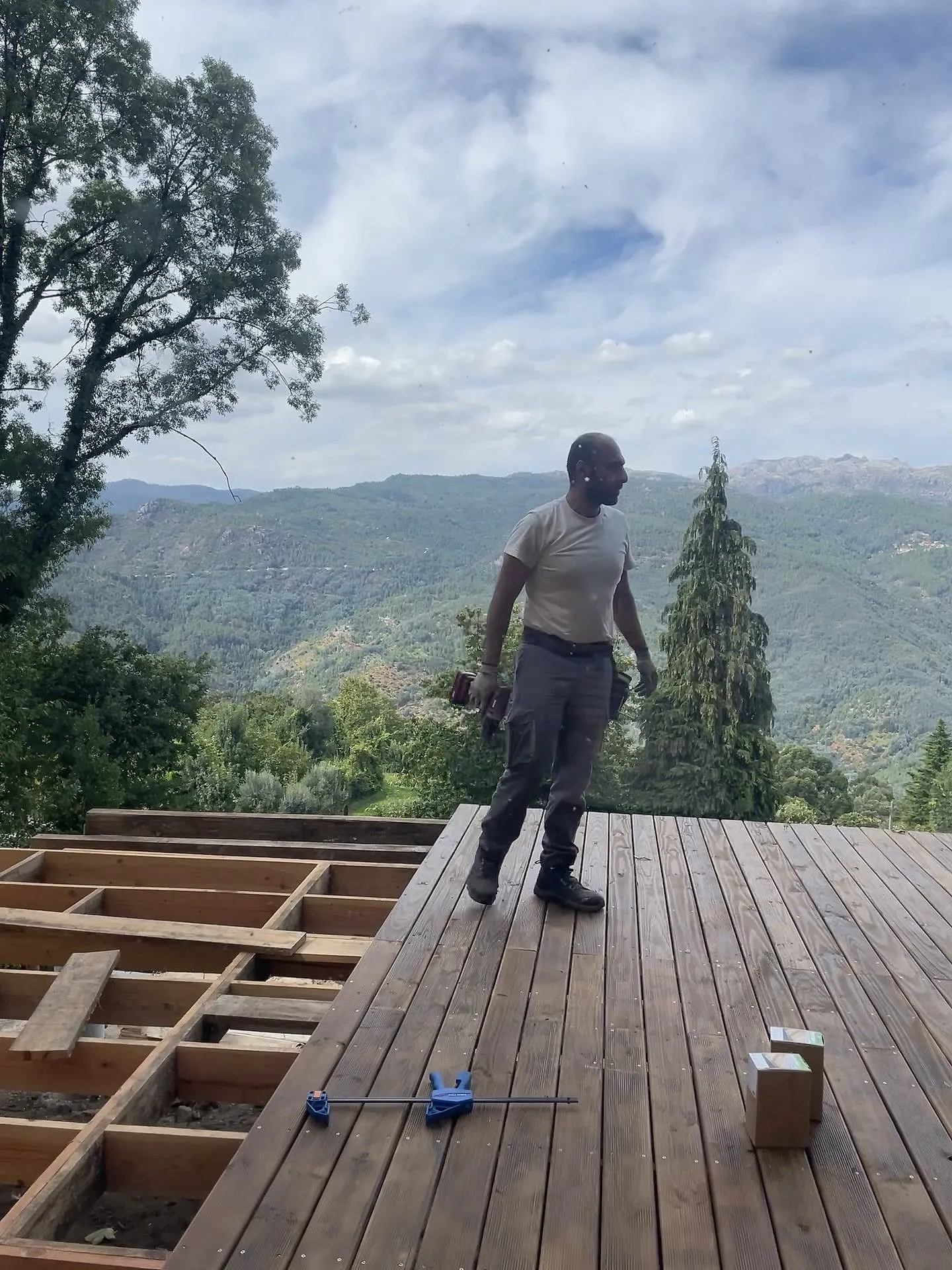 Shahin standing on a half-finished deck with mountains behind